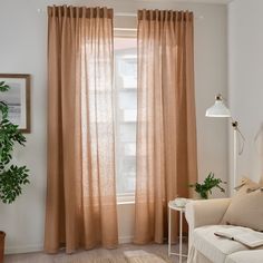 a living room with a couch, chair and window covered in sheer curtaines next to a potted plant