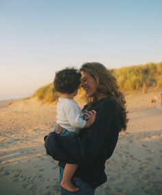 a woman holding a child on top of a sandy beach