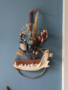 a wall hanging with flowers and other items on it's side against a blue wall