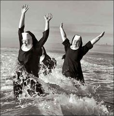 black and white photograph of two women in the ocean with their arms up, both wearing nun costumes