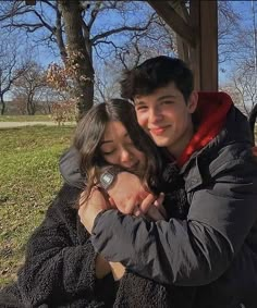 a man and woman hugging each other in front of a park bench on a sunny day