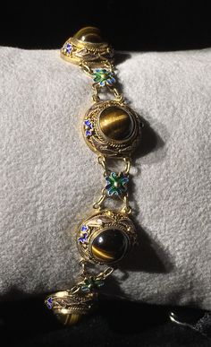 A very beautiful example of Chinese gold gilt on silver bracelet. This bracelet has bezel set round polished Tigereye stones With Enameling top and bottom and Flower links in between. Round tigereye cabochons measure 8mm with a Twist edge. There are 7 major links each set with Tigereye gold gilding all in tact . With 7 Alternate Enameled flower links . What a great gift for her absolutely near mint condition. Could become your family Heirloom . Get box with Purchase. Antique Gemstone Bracelets, Antique Round Gemstone Bracelets, Antique Gold Cabochon Bracelets, Antique Gold Bracelets With Cabochon, Victorian Gold Bracelets With Cabochon, Antique Jeweled Jewelry, Ornate Gold Oval Cabochon Jewelry, Gold Vintage Cabochons, Ornate Cabochon Bracelet Jewelry