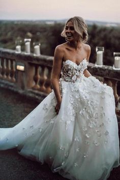 a woman in a white wedding dress standing on a balcony looking at the camera and smiling