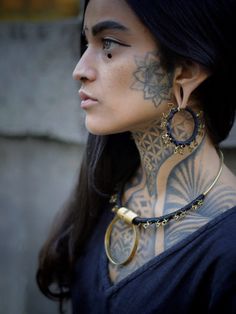 a woman with tattoos on her face and neck is looking off to the side while wearing large hoop earrings