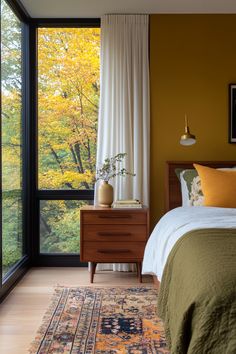 a bedroom with a bed, dresser and window overlooking the trees in the fall season