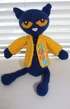 a crocheted blue and yellow cat sitting on top of a window sill