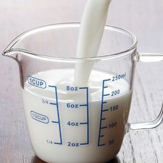 a glass measuring cup filled with milk being poured into it on top of a wooden table