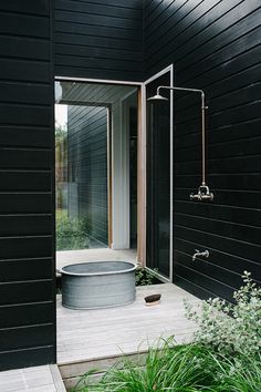 an outdoor shower in the middle of a garden area with black walls and wooden flooring