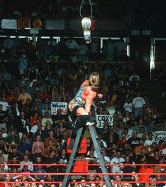 a woman standing on top of a ladder in front of a crowd at a wrestling match