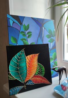 a painting on a table next to a chair and potted plant in front of a window