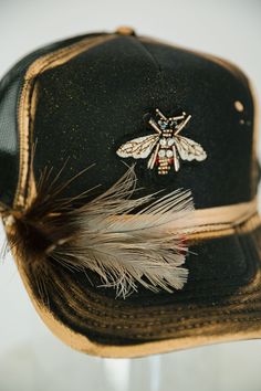 Look sharp and show off your style with this GOLDEN BEE BLACK TRUCKER HAT. This unique hat features a black trucker hat with gold accents, a gold bee patch, and a black and white feather combo that is sure to turn heads! Rock this hat and look cool and stylish - no bee-lieving required! This is a made-to-order item. All customized orders are currently shipping within 14 business days. To receive item quicker, expedited shipping is available at checkout. Black And White Feather, Custom Baseball Hats, Dope Hats, Black Trucker Hat, Unique Hats, Gold Bee, White Feather