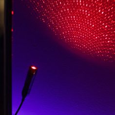 a red light shines brightly on the wall next to a black object in front of it