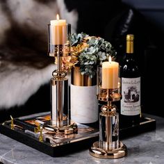 two candles are sitting on a tray next to some wine bottles and a vase with flowers