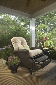 a chair and ottoman on a porch with flowers in the vases next to it