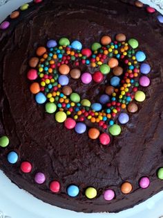 a cake with chocolate frosting and colorful candies in the shape of a heart