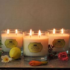 three lit candles sitting on top of a table next to some flowers and a lemon