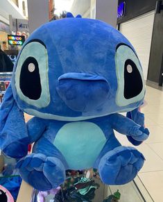 a blue stuffed animal sitting on top of a glass shelf next to other items in a store