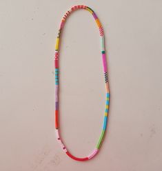 a multicolored beaded necklace is displayed on a white surface with an orange, yellow, and pink cord