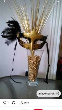 a masquerade mask sitting on top of a vase filled with gold and black feathers