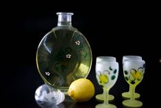 three wine glasses sitting next to a bottle and two lemons on a black surface