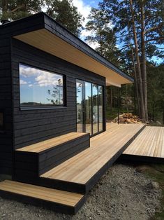 a small black house sitting on top of a wooden deck next to a forest filled with trees