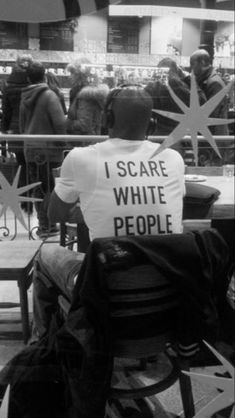 a man sitting in a chair with a sign on his back that says i scare white people