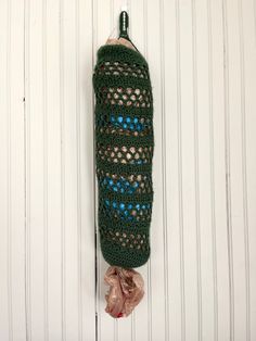 a green crochet bag hanging on a white wall with a brown ribbon around it