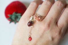 a person's hand with a ring on it and a strawberry in the background