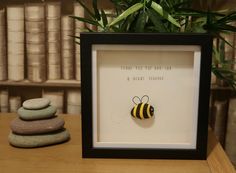 there is a framed picture with a bee on it next to some rocks and a potted plant