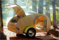 an old camper converted into a bed in the woods with its hood open to let people sleep inside