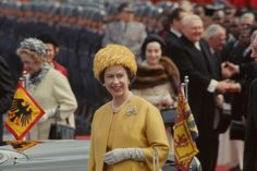 an older woman in a yellow coat and hat standing next to a car with flags on it