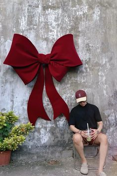 a man sitting on a chair next to a wall with a large red bow hanging from it's side