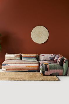 a living room with a couch, rug and potted plant on the floor in front of an orange wall