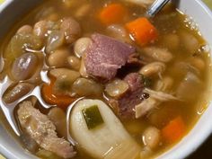 a bowl of soup with meat, beans and carrots