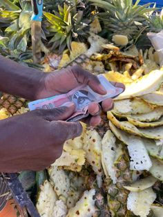 a person is peeling an item from a pile of pineapples and other fruit