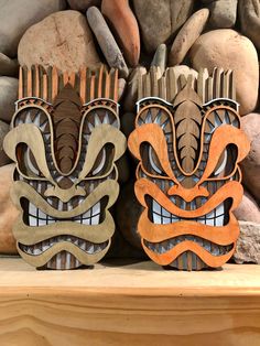 two wooden masks sitting next to each other on top of a shelf in front of rocks