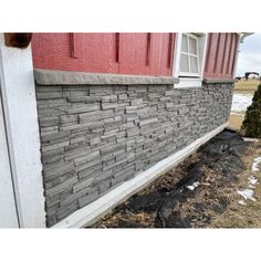 the side of a house with snow on the ground and grass growing next to it