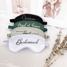 three bridesmaid sleep masks sitting on top of a white table next to flowers