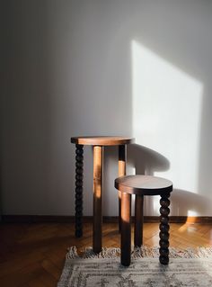 two wooden tables sitting next to each other on top of a rug in front of a white wall