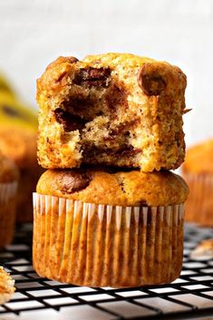 two chocolate chip muffins stacked on top of each other with bananas in the background