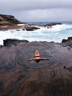 a woman laying on top of a rocky beach next to the ocean