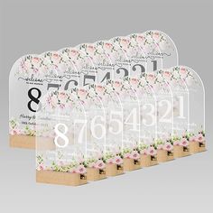 four clear acrylic signs with flowers and numbers on each one, in front of a gray background