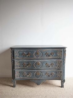 an old blue dresser with ornate carvings on the front and drawers, against a white wall