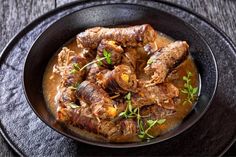 a bowl filled with meat and sauce on top of a wooden table