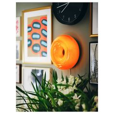 an orange donut is hanging on the wall next to some pictures and flowers with a clock in the background