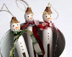 three snowmen made out of toothpicks sitting in a tin can filled with candy canes