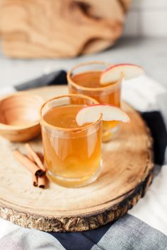 two glasses filled with apple cider on top of a wooden tray