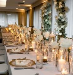 a long table is set with candles and white flowers in vases on the tables