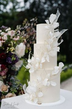 a three tiered white wedding cake with flowers on the top and bottom, sitting on a table