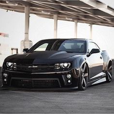 a black chevrolet camaro is parked in front of a parking garage with its lights on